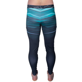 A person is standing barefoot, shown from the back, wearing Icelantic’s 22/23 Mens WiKmax Baselayer Full Bottoms, which feature a tight fit, dark fabric with blue and teal geometric patterns, and a branded waistband made from innovative WIKMAX material. The background is white and uncluttered.