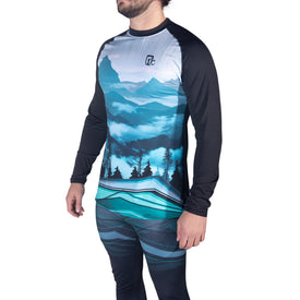 A person wearing the Icelantic 22/23 Mens WikMax Baselayer Top from the Pioneer Collection, showcasing a blue and black mountain landscape design. Only the torso and upper legs are visible; the shirt is made with advanced WIKMAX fabric for optimal comfort. The background is white.