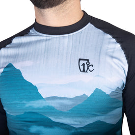 A person is shown wearing the Icelantic 22/23 Mens WikMax Baselayer Top, which features blue mountain graphics and a small black logo on the chest. Made from innovative WIKMAX fabric, the shirt is displayed in an image cropped at the neck against a white background.