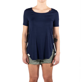 A person is shown from the upper body to upper legs, standing against a white background and facing forward, wearing the Icelantic Skis Eco Bamboo T in navy paired with light-colored denim shorts.