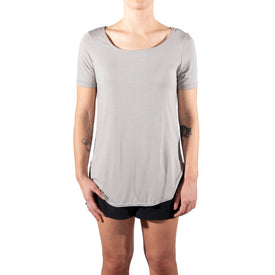 A person stands against a white background, wearing the Icelantic Skis Eco Bamboo T in Sand and black shorts. Their arms are relaxed at their sides, and their face is not visible in the image.